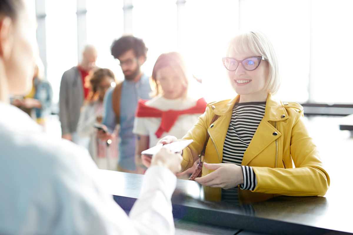 Young blonde woman giving documents while passing check in in airport in backlit